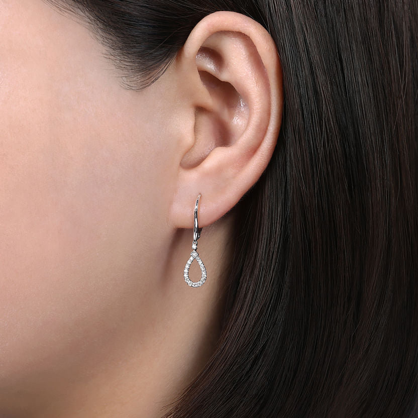 Close-up of a person wearing Gabriel & Co 14K White Gold Pear Shaped Diamond Drop Earrings, featuring sparkling diamonds that dangle just below the earlobe against straight, dark brown hair.
