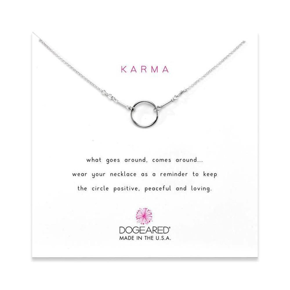 A silver necklace with a circular pendant is displayed on a white card. The card features the words "Original Karma" in red at the top and a message below: "what goes around, comes around... wear your 16\" w/2\" necklace as a reminder to keep the circle positive, peaceful, and loving." The bottom of the card includes the logo "DOGEARED MADE IN THE USA.