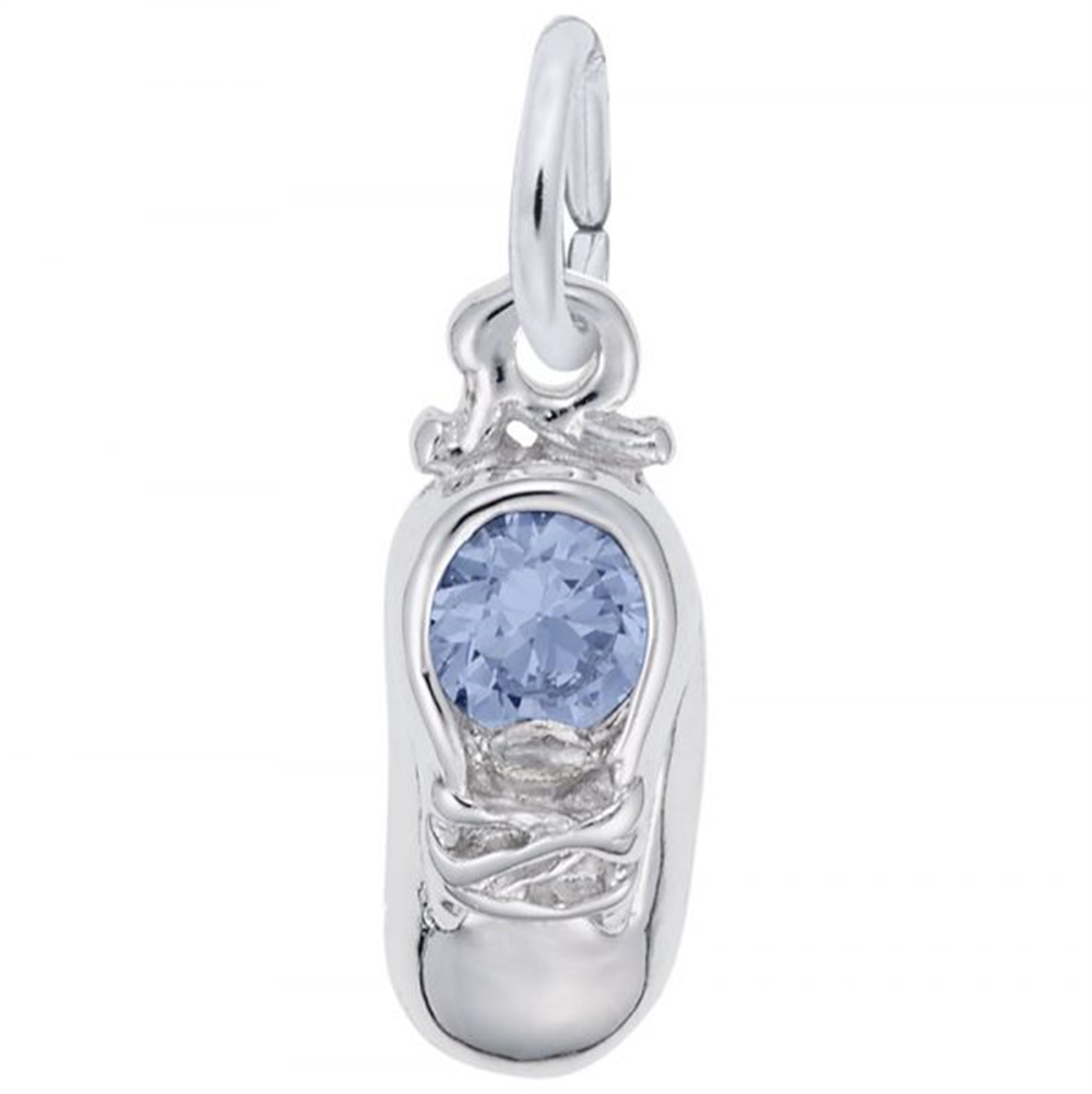 The March Baby Shoe Charm by Rembrandt Charms is a sterling silver charm in the shape of a baby shoe, featuring a round, light blue gemstone at the center. The charm boasts detailed shoelaces and includes a small loop at the top for easy attachment to a bracelet or necklace, making it an ideal March birthstone accessory.