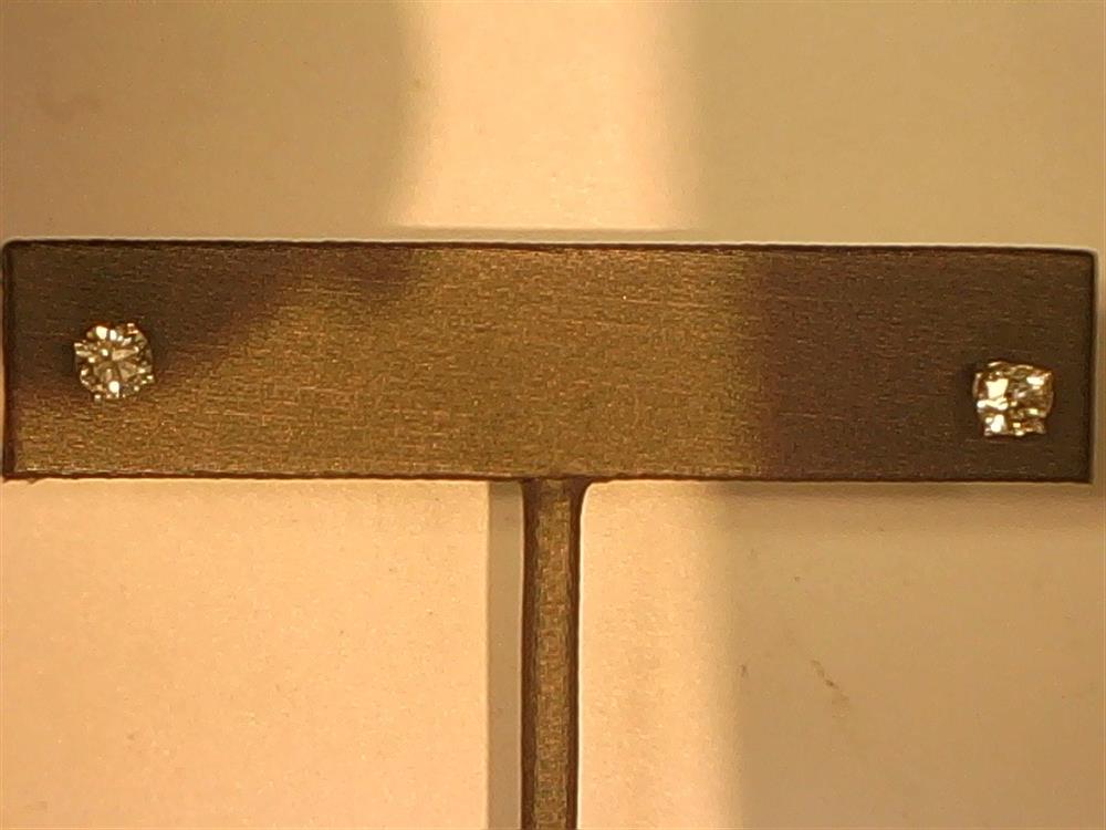 A pair of Veer 14KW 4-prong / 0.50ctw Stud earrings is displayed on a metallic stand against a neutral background. The round-cut diamonds are set in four-prong, 14KW settings. The lighting highlights the sparkle of the diamonds, showcasing their timeless elegance and brilliance.