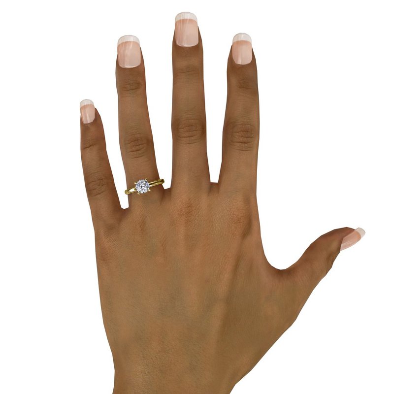 A hand with manicured nails displays the FANA 14K Yellow Gold Classic Round Cut Solitaire Engagement Ring, featuring a single round diamond, shown on the ring finger against a plain white background.
