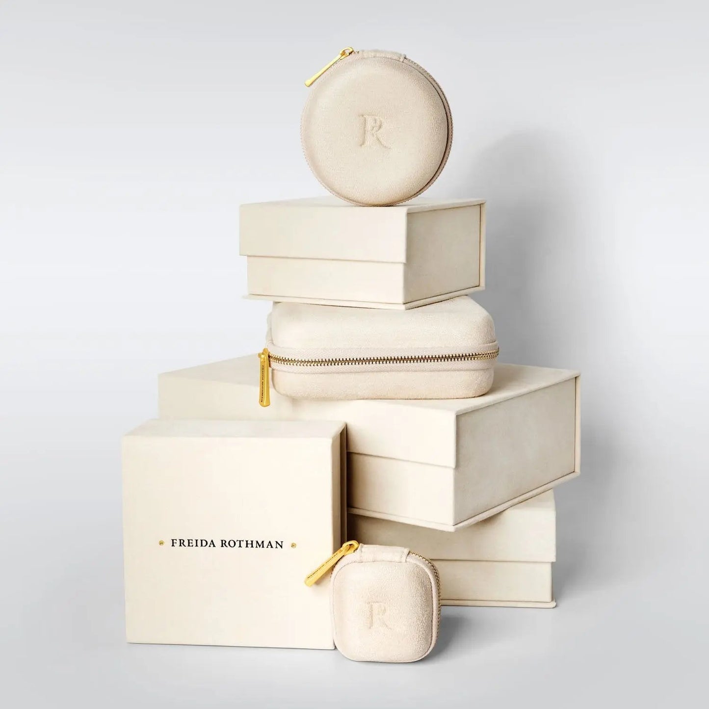 A stack of elegant beige jewelry boxes showcases treasures like the Classic Pave Hinged bangle. The largest box features "Freida Rothman" in bold black letters, while others have rounded edges and gold zippers, ideal for a YZB080047B-HG.