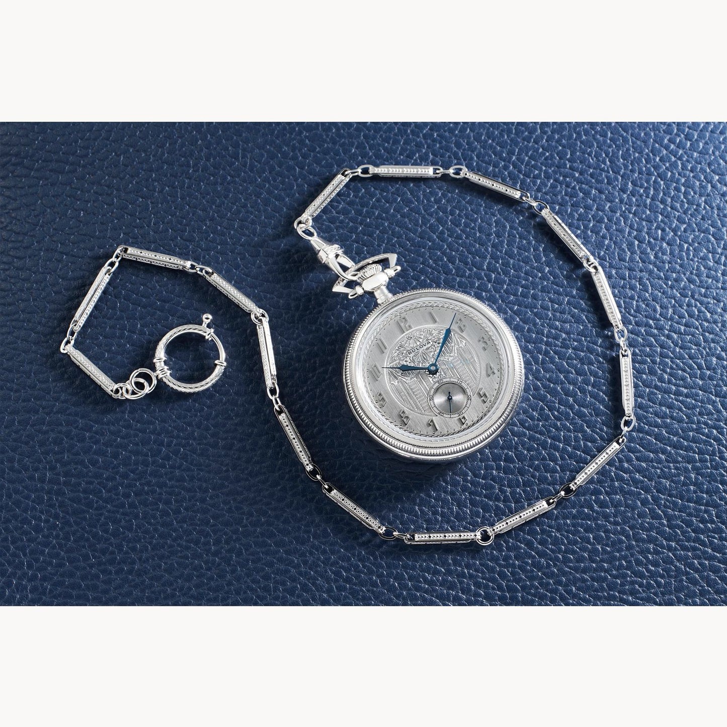 A Bulova Watch Company Limited Edition Silver-Tone Stainless Steel Chain Pocket Watch with a blue hand rests on textured dark blue leather.