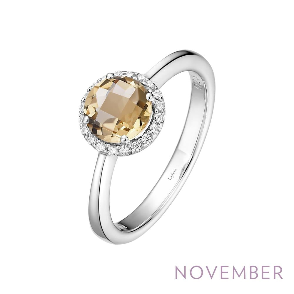 A Lafonn November Birthstone Ring featuring a round, faceted yellow gemstone at its center, surrounded by small clear stones. The word "November" is elegantly inscribed at the bottom right corner of the image.