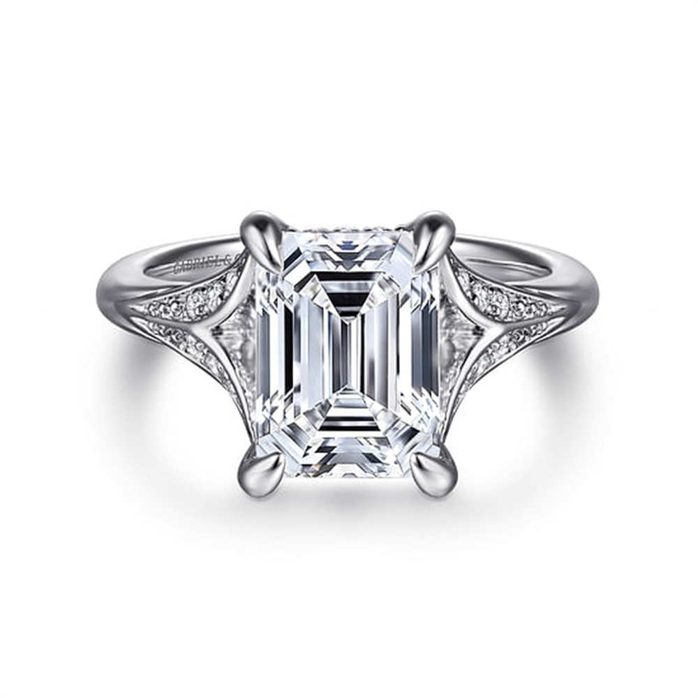 The Gabriel & Co 14K White Gold Split Shank Emerald Cut Diamond Engagement Ring features a stunning emerald-cut center stone with delicate diamond accents, all beautifully set in white gold.