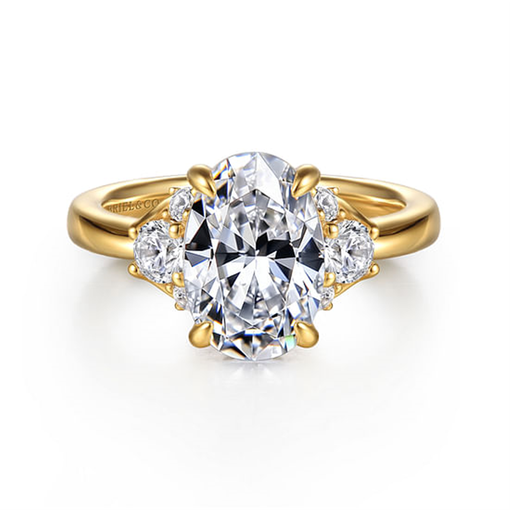 The Gabriel & Co 14K Yellow Gold Oval Lotus Diamond Engagement Ring features a 10.5x7 mm clear oval lotus diamond center stone, accented by two smaller heart-shaped clear stones on each side.