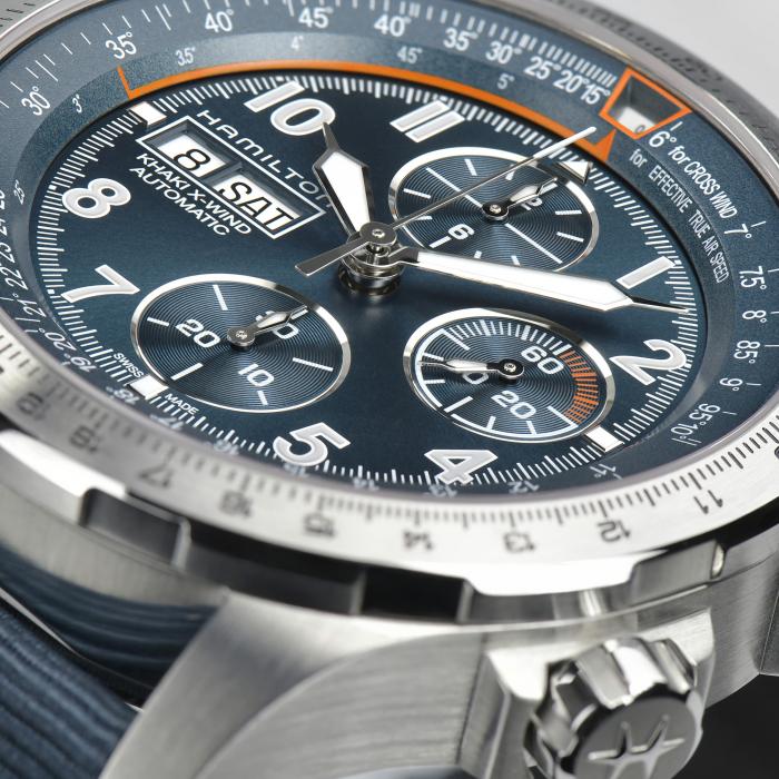 Close-up of a Hamilton Khaki Aviation X-Wind Automatic Chronograph Watch featuring a blue dial. This high-performance timepiece includes three sub-dials for measuring seconds, minutes, and hours, along with day and date displays. The bezel is adorned with a tachymeter scale, complemented by a polished stainless steel case.