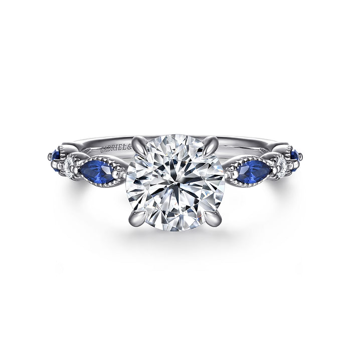 The Gabriel & Co 14K White Gold Round Sapphire and Diamond Engagement Ring features a 2 carat center diamond, marquise-cut blue sapphires on each side, and an ornate band with sparkling diamond accents.