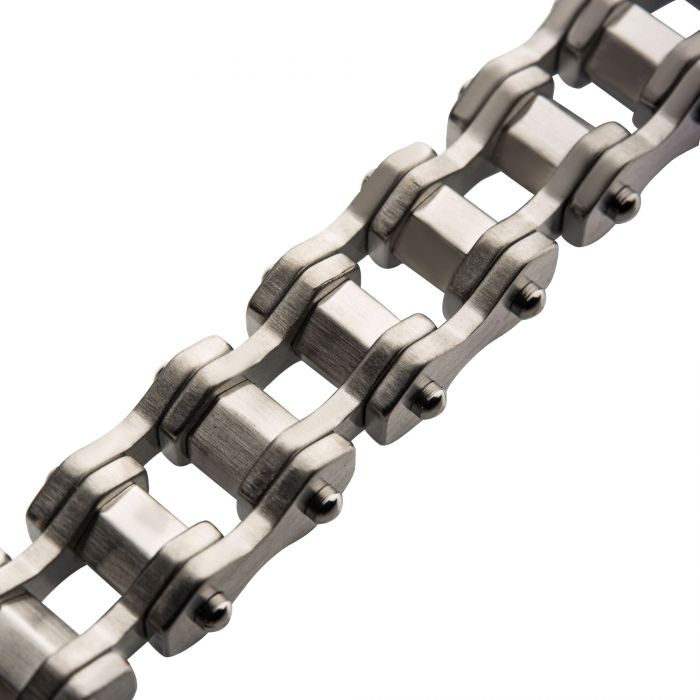 A close-up of a metallic roller chain used in machinery or bicycles. The INOX Steel Bike Chain Bracelet features interlocked, polished silver links and shiny rivets, showcasing precise craftsmanship and rugged durability. The image captures the bracelet at an angle, emphasizing its texture and design.
