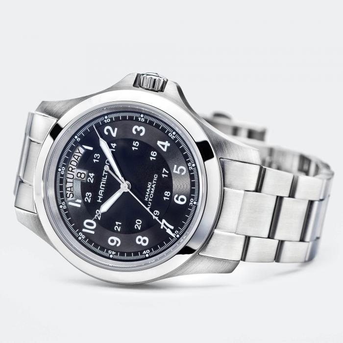 A Hamilton Khaki Field King Automatic wristwatch with a stainless steel band and a black dial featuring both 12-hour and military time markings, a day-date display at the 12 o'clock position, and luminous hands. The watch is positioned at an angle against a light grey background.