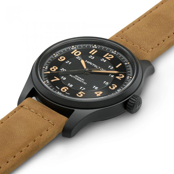 A close-up of the Hamilton Khaki Field Titanium Automatic Watch showcases its black round face adorned with Arabic numerals and a sleek black bezel. The wristwatch features brown leather straps, while beige hour markers and additional 24-hour military time indicated inside the primary numerals encapsulate the essence of military-inspired design.