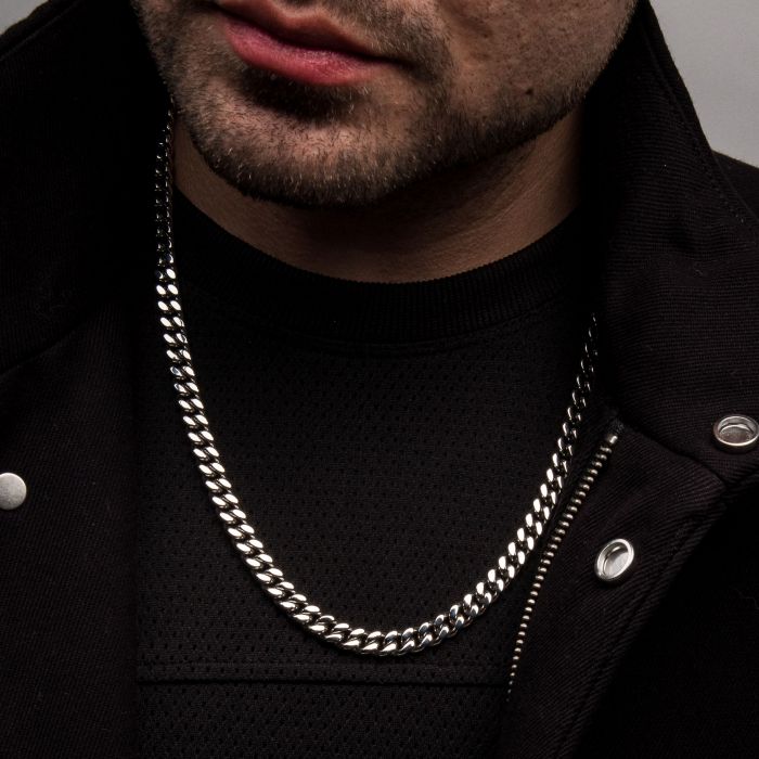 A close-up of a man wearing the 8mm Steel Miami Cuban Chain | 20" by INOX and a black jacket. The man's face is partially visible, with the focus on his lips and chin. The texture of his jacket and the clasp of the INOX chain stand out prominently.