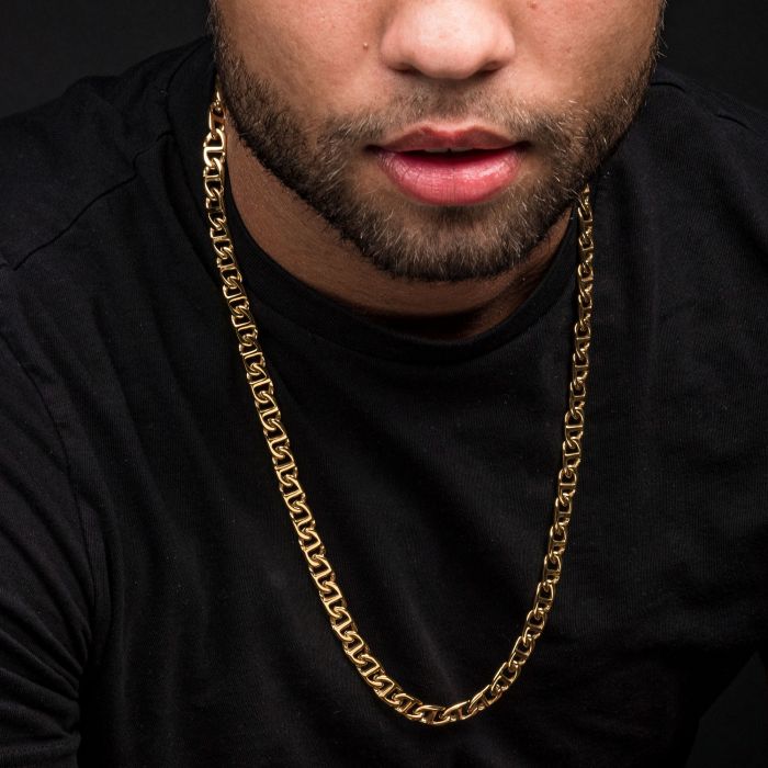 A close-up view of a person wearing a black shirt and an 8mm 18K Gold Plated Mariner Link Chain by INOX, measuring 22 inches. The person's face is partially visible, focusing on the lips, beard, and neck. The background is dark, emphasizing the gold chain.