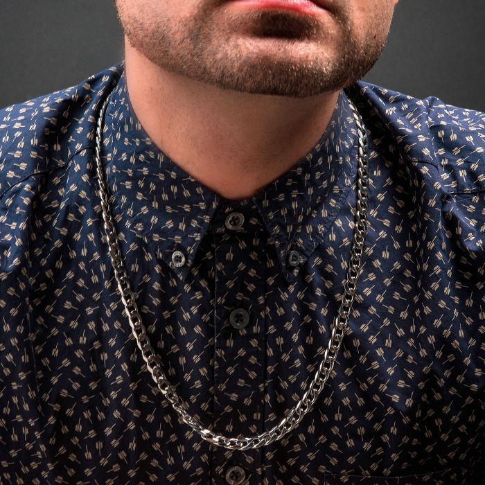 Close-up of a person wearing a dark, patterned shirt with a buttoned-up collar and an INOX 6mm Steel Diamond Cut Curb Chain | 22". The image focuses on the lower part of their face, neck, and upper chest, with a dark background.