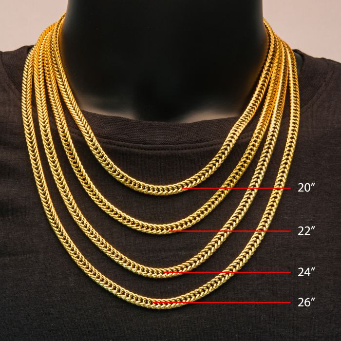A display showcases five gold chains of different lengths on a black mannequin bust. The lengths of the 18K Gold Plated chains, including the 6mm 18K Gold Plated Foxtail Chain by INOX at 22 inches, are marked with red lines and white text: 20 inches, 22 inches, 24 inches, and 26 inches. The Men's Stainless Steel Necklaces are arranged from shortest to longest.