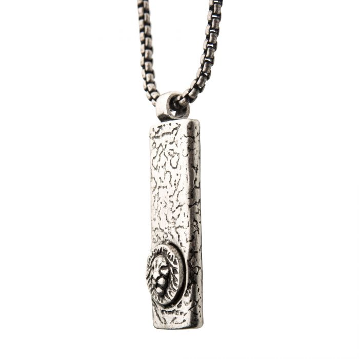 A close-up of the Stainless Steel Silver Plated Dog Tag Pendant with Lion Head Inlay, hanging from a steel box chain by INOX. The rectangular, men's dog tag has a textured surface resembling rough stone and features an engraved circular emblem with a detailed lion head design in the center.