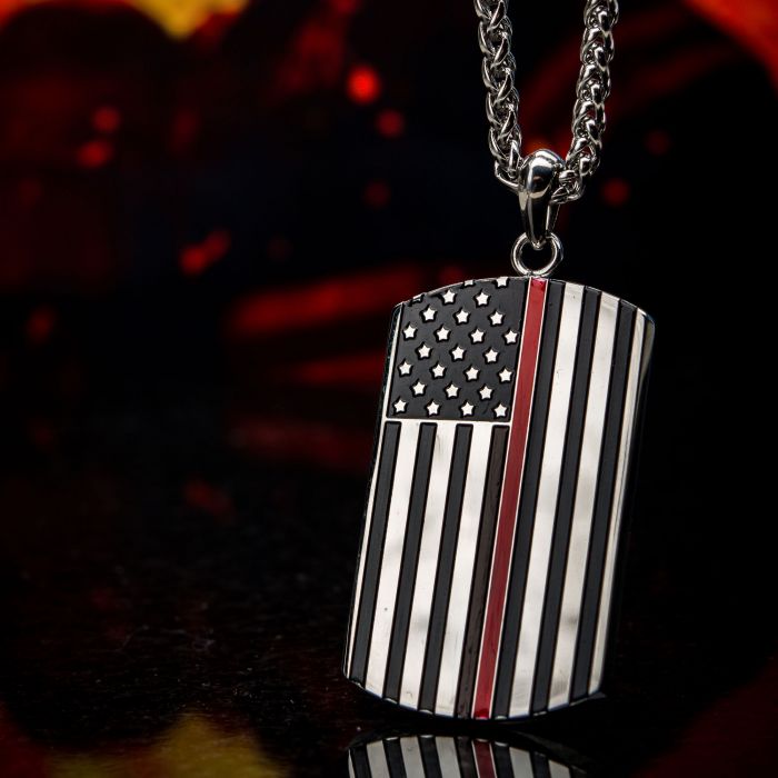A close-up image of the INOX Stainless Steel with Thin Red Line American Flag Firefighter Military dog tag depicts the American flag in a black and white color scheme with a single red stripe. The pendant, part of an INOX stainless steel necklace, stands out against a dark background with red accents, highlighting its design.