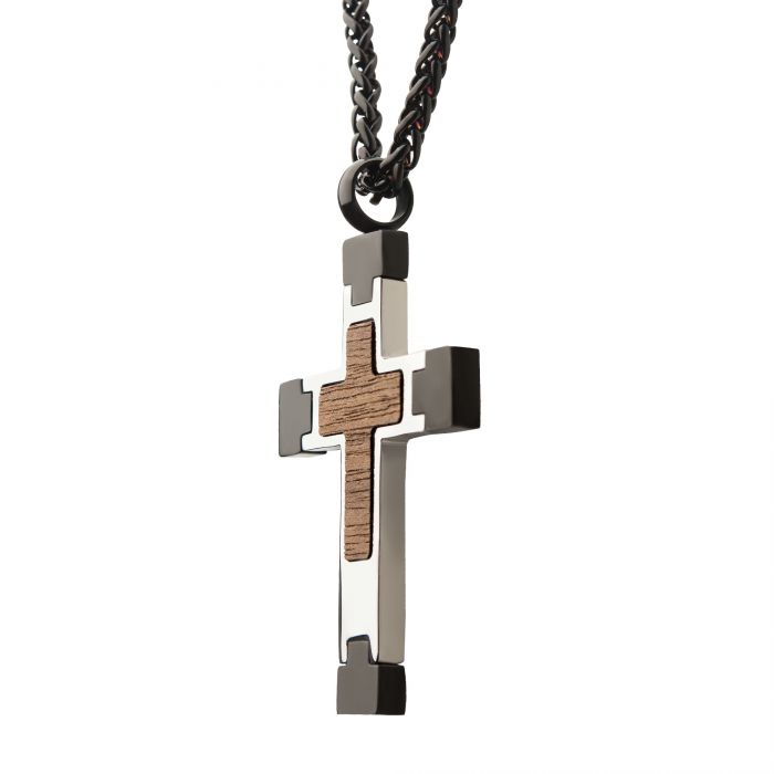 The INOX Steel Cross Pendant with Walnut Wood Inlay hangs elegantly from a thick black wheat chain. The pendant showcases a smaller cross shape within the walnut wood inlay, creating a striking contrast against the polished metal surrounding it. The chain is sturdy and linked, adding to its robust appearance.
