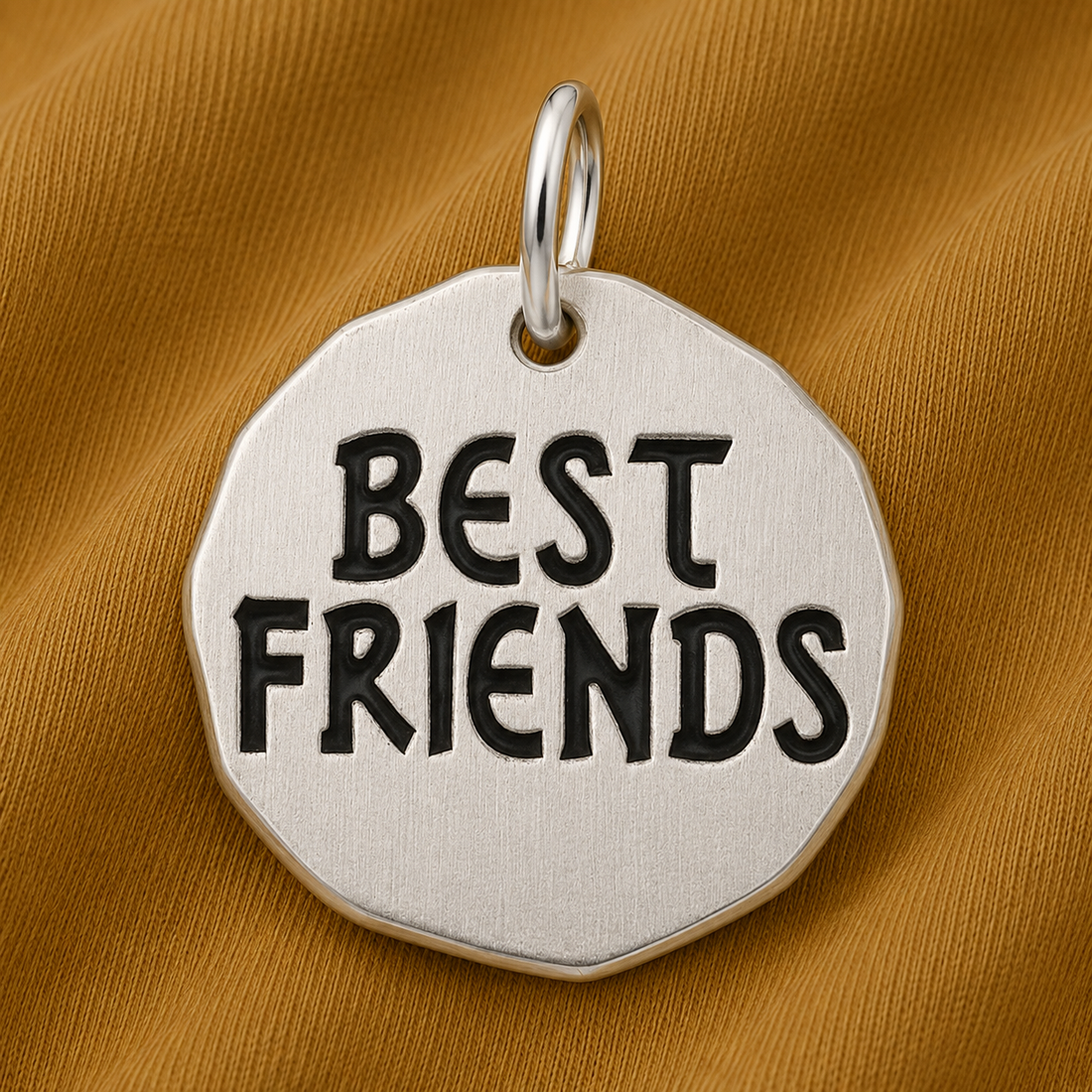 The Best Friends Tag Charm—Sterling Silver by Rembrandt Charms rests on a textured gold-brown fabric background, making it a meaningful piece of friendship jewelry and the perfect gift for best friends.