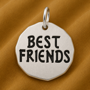 The Best Friends Tag Charm—Sterling Silver by Rembrandt Charms rests on a textured gold-brown fabric background, making it a meaningful piece of friendship jewelry and the perfect gift for best friends.