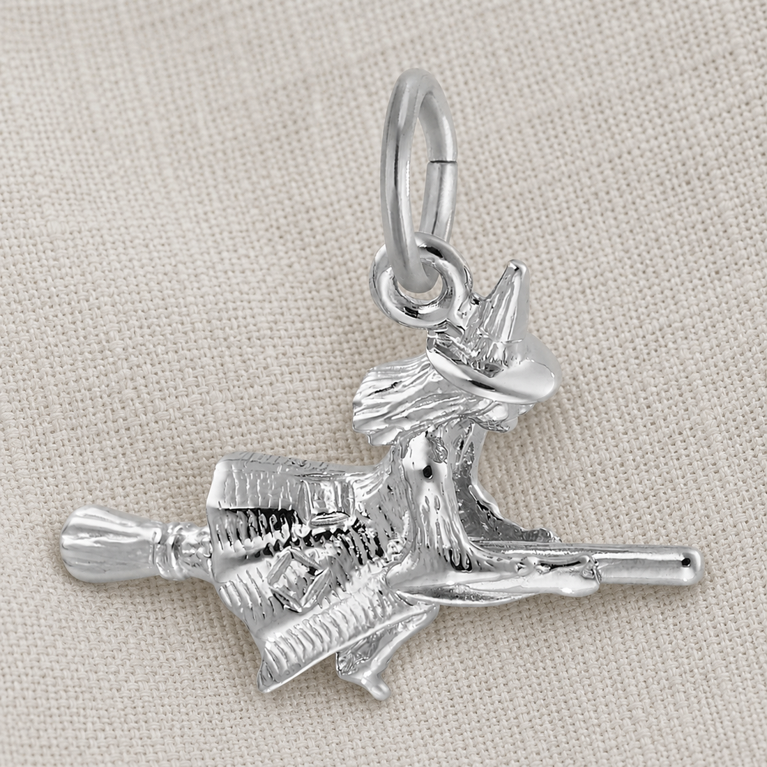 The Rembrandt Charms Witch Charm—Sterling Silver, featuring a detailed witch on her broomstick, is showcased against a light fabric background. Perfect as Halloween jewelry, this charm adds a magical touch to any collection.