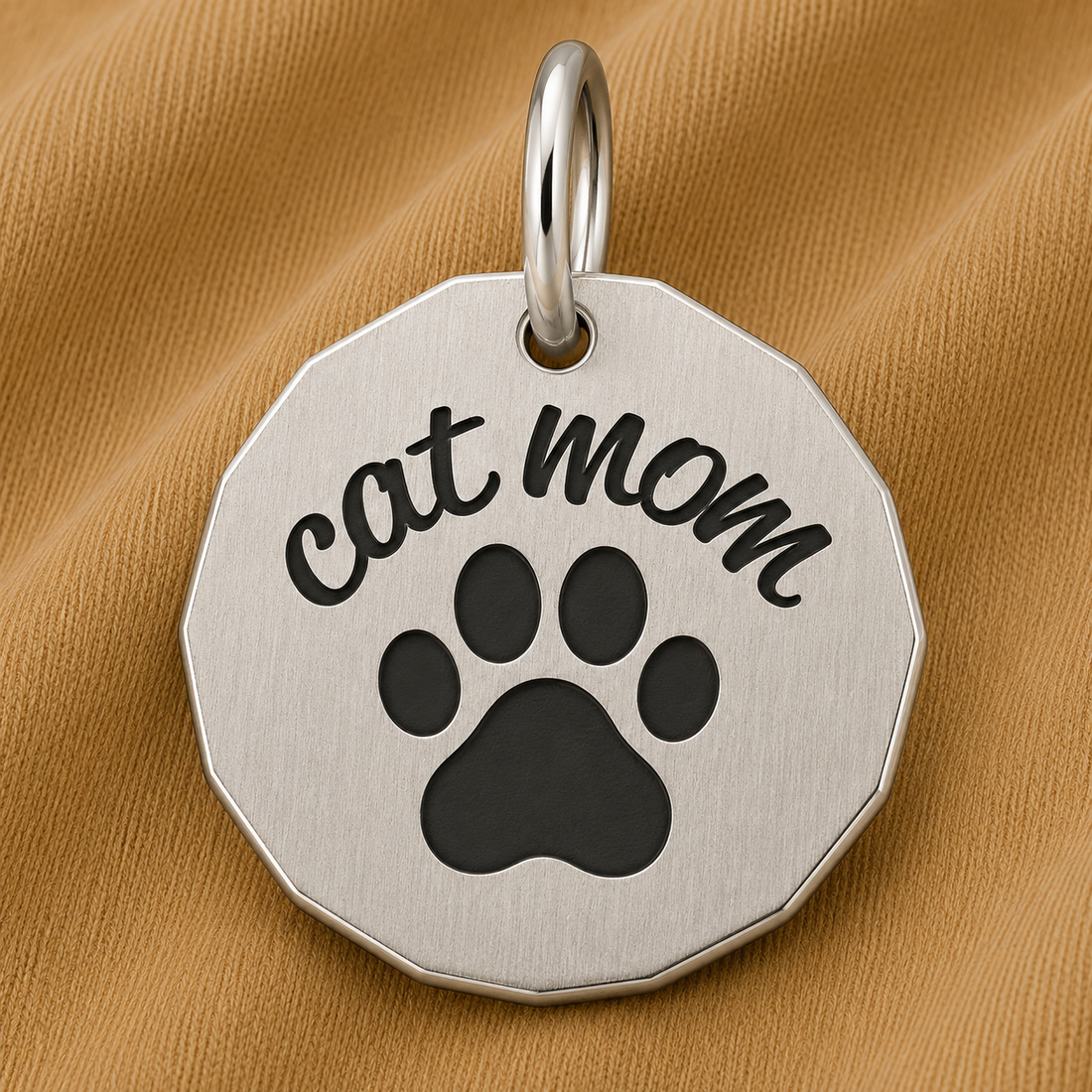 Showcase your love for your feline companion with the Rembrandt Charms Cat Mom Charm in sterling silver, featuring “cat mom” engraved above a black paw print. Displayed on a textured tan fabric background, this thoughtful piece makes the perfect paw print jewelry or an adorable cat mom gift.