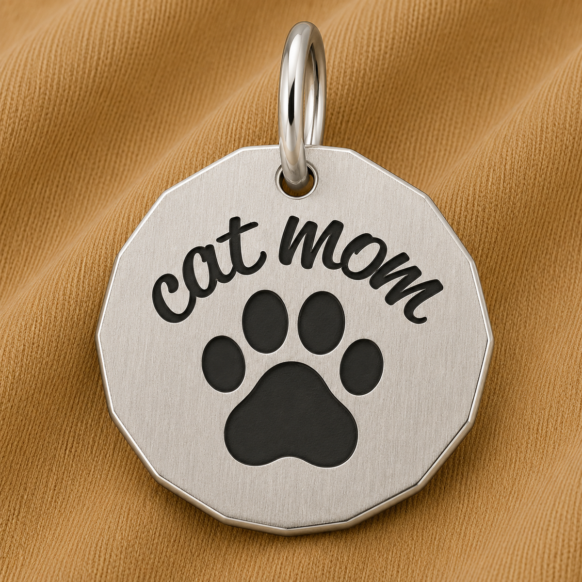 Showcase your love for your feline companion with the Rembrandt Charms Cat Mom Charm in sterling silver, featuring “cat mom” engraved above a black paw print. Displayed on a textured tan fabric background, this thoughtful piece makes the perfect paw print jewelry or an adorable cat mom gift.