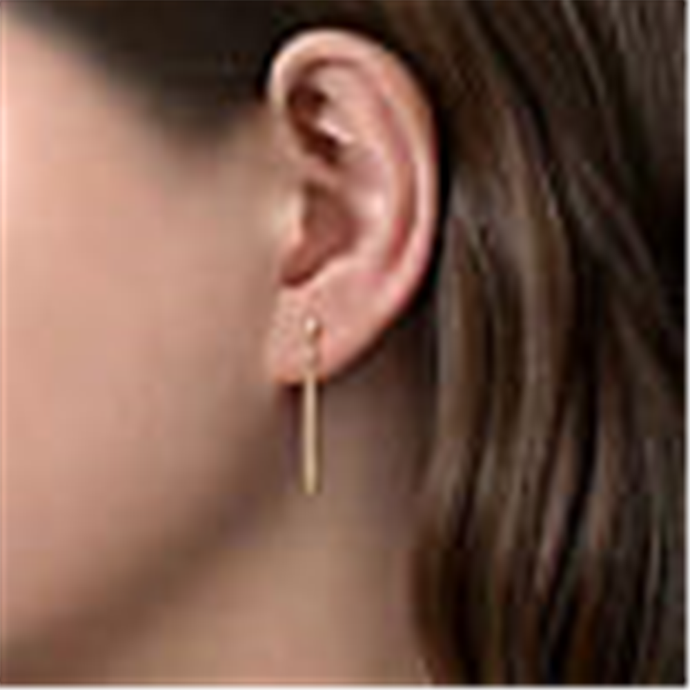 Close-up of a person's ear showcasing a single, elegant 14K Yellow Gold Diamond and Spike Drop Earring by Gabriel & Co. Part of the Contemporary Collection, it features a slim, vertical design hanging from a small hoop. The diamond drop earrings shimmer subtly under the partially covering brown hair. The background is out of focus.