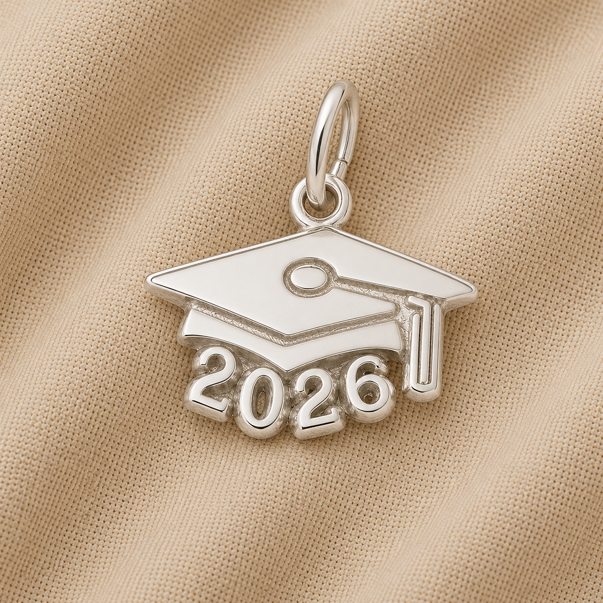 Celebrate the class of 2026 with the Rembrandt Charms Grad Cap 2026—Sterling Silver charm, featuring a mortarboard design with “2026” beneath, beautifully displayed on beige fabric—the perfect graduation gift.