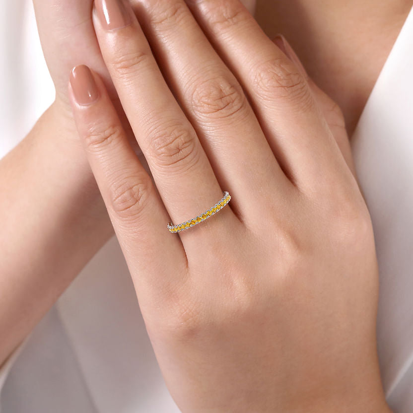 A close-up of a manicured hand wearing the Gabriel & Co 14K White Gold Citrine Stackable Ring, adorned with small yellow citrine gemstones, set against a softly blurred, light background.