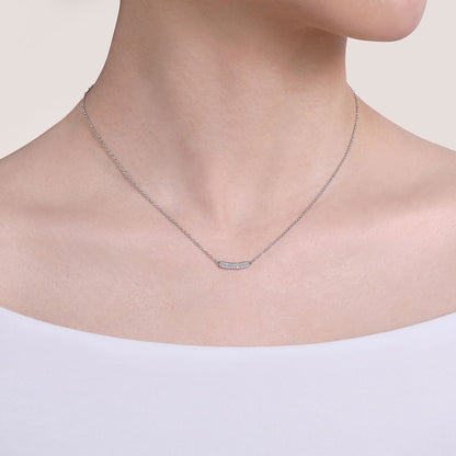 A person wears an off-the-shoulder white top and the Gabriel & Co 14K White Gold Curved Pavé Diamond Bar Necklace, featuring a delicate bar pendant on an adjustable cable chain.