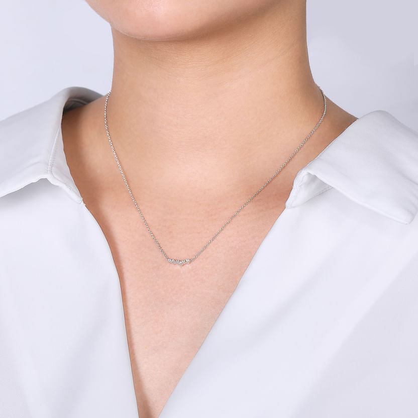 A person in a white collared shirt showcases Gabriel & Co’s 14K White Gold Diamond Constellation Bar Necklace, the delicate pendant resting just below the collarbone against a plain light background.