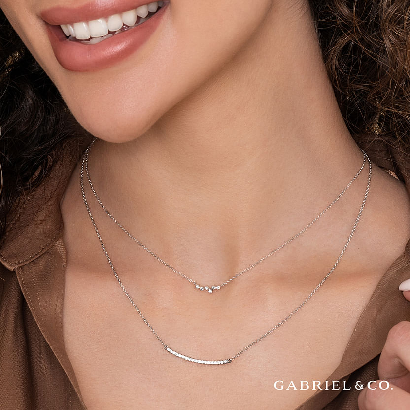 A woman smiles in a brown top, wearing the Gabriel & Co 14K White Gold Diamond Constellation Bar Necklace. The Gabriel & Co logo appears in the corner of the image captured for Avonlea Jewelers.