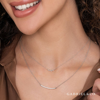 A woman smiles in a brown top, wearing the Gabriel & Co 14K White Gold Diamond Constellation Bar Necklace. The Gabriel & Co logo appears in the corner of the image captured for Avonlea Jewelers.