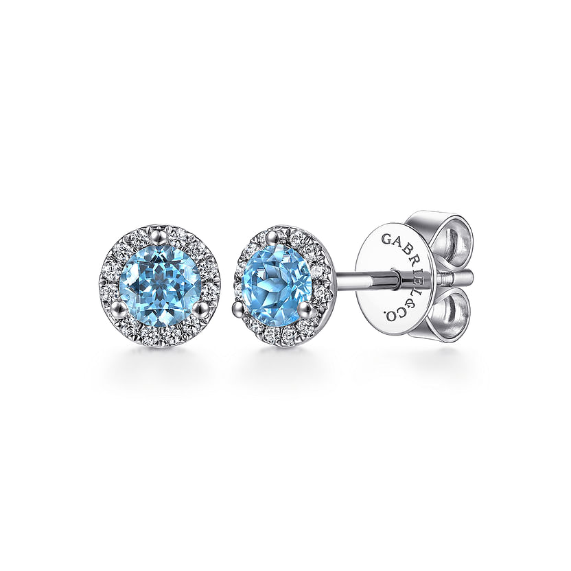 The 14K White Gold Diamond Halo Swiss Blue Topaz Stud Earrings by Gabriel & Co feature round Swiss Blue Topaz gemstones with a diamond halo and butterfly backs engraved with "GABRIEL & CO.