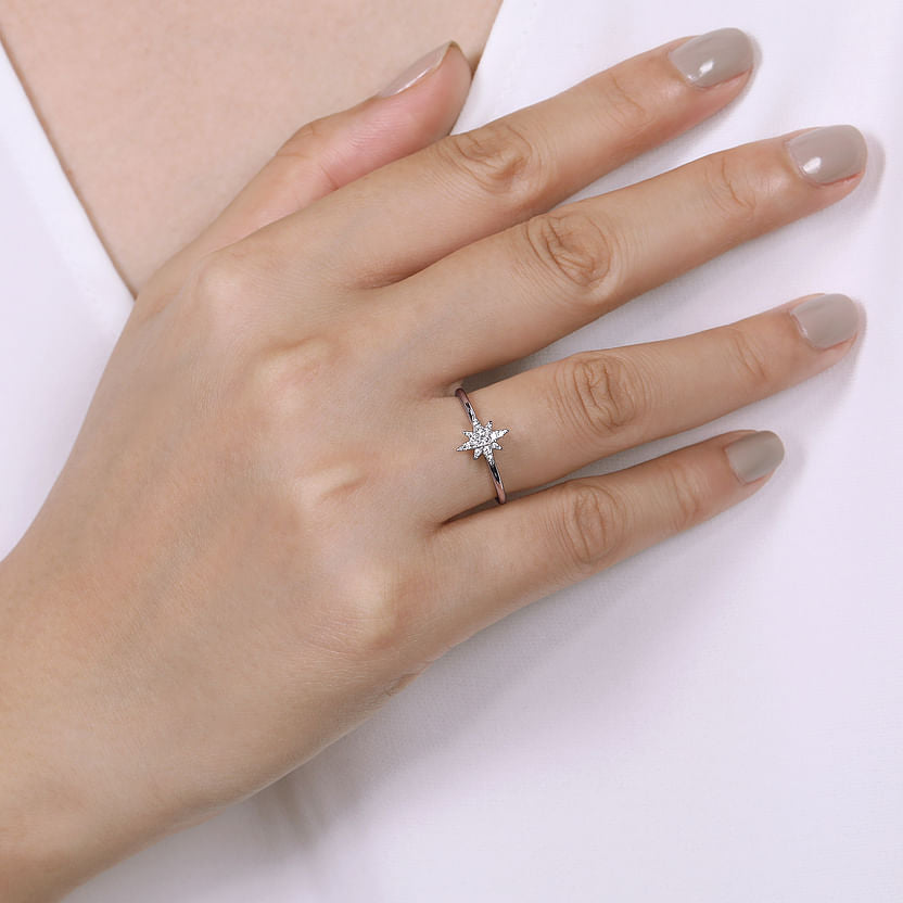 A hand with manicured nails wears the Gabriel & Co 14K White Gold Diamond Starburst Ring, featuring a star-shaped diamond and celestial-inspired design, resting gracefully against a white garment.