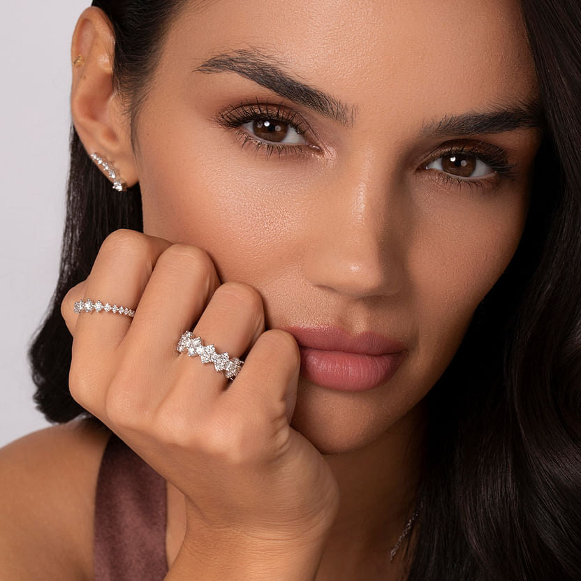 A woman with long dark hair and flawless makeup poses in a sleeveless top, displaying the Gabriel & Co 14K White Gold Graduating Diamond Classic Ladies Ring on her finger, her hand elegantly near her face.