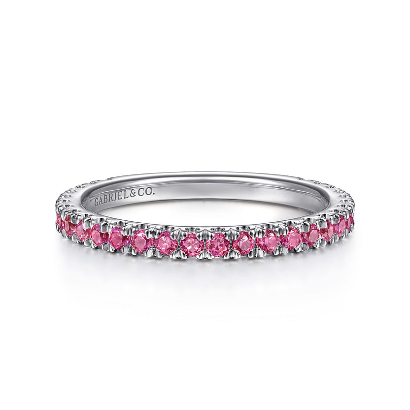 A delicate 14K white gold ruby stackable ring by Gabriel & Co, featuring small round pink gemstones evenly spaced around the band and "GABRIEL & CO." engraved inside.