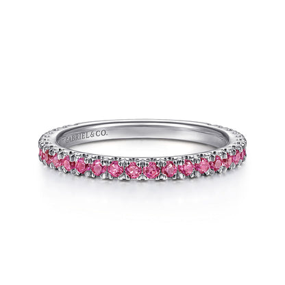 A delicate 14K white gold ruby stackable ring by Gabriel & Co, featuring small round pink gemstones evenly spaced around the band and "GABRIEL & CO." engraved inside.