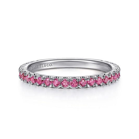 A delicate 14K white gold ruby stackable ring by Gabriel & Co, featuring small round pink gemstones evenly spaced around the band and "GABRIEL & CO." engraved inside.