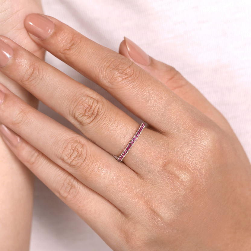 A hand with neatly manicured nails wears a Gabriel & Co 14K White Gold Ruby Stackable Ring on the middle finger, gently resting against a white shirt.