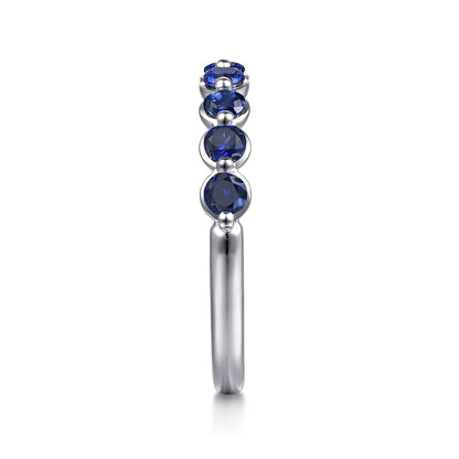 A side view of the Gabriel & Co 14K White Gold Sapphire Stackable Ring displays five round blue sapphires set in a vertical row along the white gold band, shown against a white background.