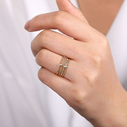 A hand with manicured nails showcases the Gabriel & Co 14K Yellow Gold Bezel Set Diamond Station Layered Ring, featuring three diamond-accented bands. The person is dressed in a white garment.
