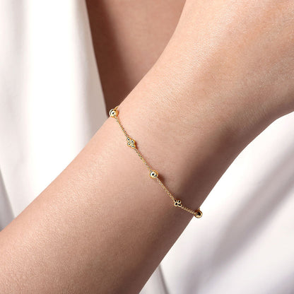 A close-up of a woman's wrist wearing the Gabriel & Co 14K Yellow Gold Bujukan Beads Station Bracelet, paired with a white sleeveless top.