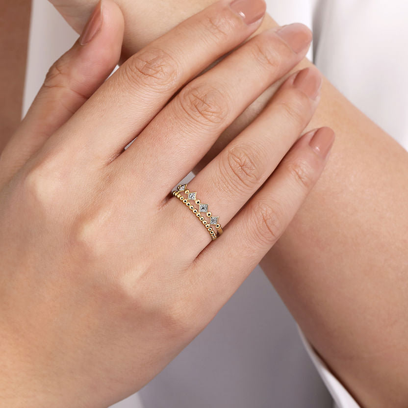A close-up of a hand wearing the Gabriel & Co 14K Yellow Gold Bujukan Diamond Easy Stackable Ring, featuring delicate diamonds, stands out against manicured nude nails and a white garment.