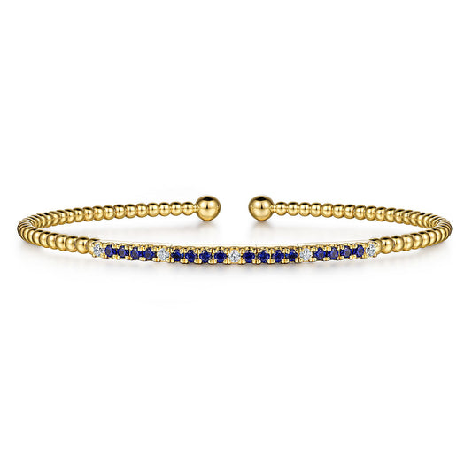 The Gabriel & Co 14K Yellow Gold Bujukan Diamond and Blue Sapphire Split Bangle features beaded detailing, a central bar with alternating sapphires and diamonds, and two round gold end caps.