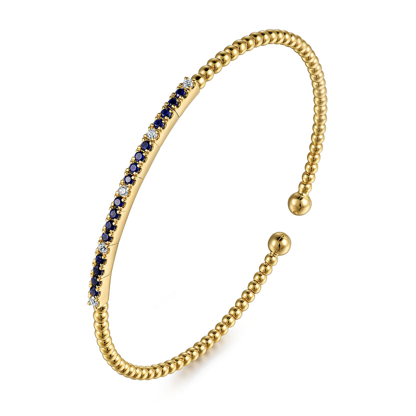 The Gabriel & Co 14K Yellow Gold Bujukan Diamond and Blue Sapphire Split Bangle features a row of blue sapphires and diamonds set atop an open gold bangle with beaded detailing and rounded ends.