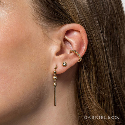 Close-up of a woman's ear with three gold earrings: a 14K yellow gold hoop on the helix, a clear stud on the lobe, and 14K Yellow Gold Bujukan Drop Earrings by Gabriel & Co. "GABRIEL & CO." appears in the lower right corner.