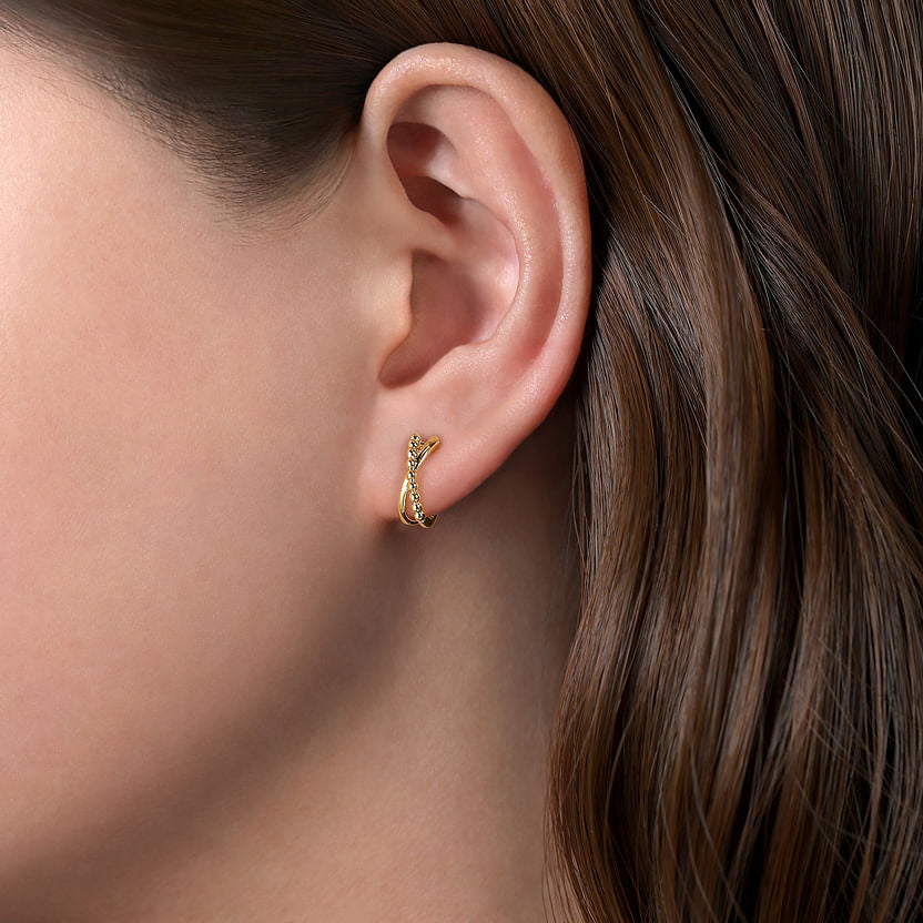 Close-up of a woman's ear with long brown hair, wearing a 14K Yellow Gold Bujukan Twisted Huggie Earring by Gabriel & Co, which follows the natural contour of her earlobe.