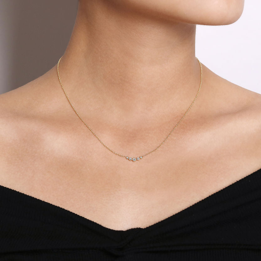 A close-up of a person wearing the Gabriel & Co 14K Yellow Gold Curved Diamond Bar Necklace, featuring sparkling diamonds and paired with an off-shoulder black top for vintage-inspired elegance.
